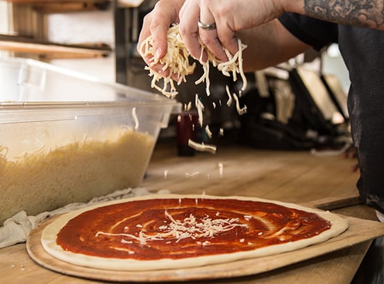 Hands dropping mozzarella on a pie